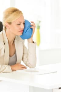 Businesswoman having toothache she is icing her jaw with a blue ice pack