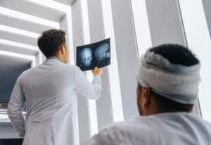 Healthcare professional young doctor examining and analyzing x-ray CT Scan test for facial injuries to the human head results of the patients skull with his patient in a medical hospital clinic.