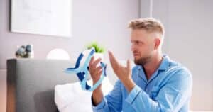 30-year-old man angry holds up part of CPAP machine in frustration, ready to try a better surgical solution for sleep apnea.