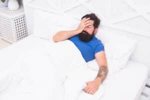 Bearded man lies in bed half asleep after a night of lousy sleep due to obstructive sleep apnea.
