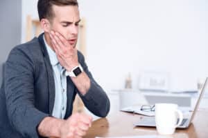 Man working in an office winces from jaw pain at his desk.