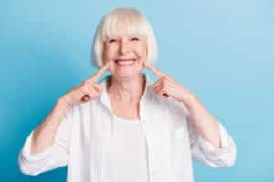 Cute woman in her 60s flashes a big smile after successful dental implant treatment.